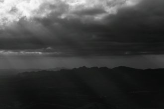 Montanhas de Minas Gerais sob nuvens densas e dramáticas, em uma paisagem em preto e branco.