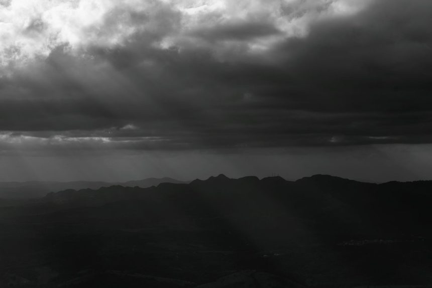 Montanhas de Minas Gerais sob nuvens densas e dramáticas, em uma paisagem em preto e branco.