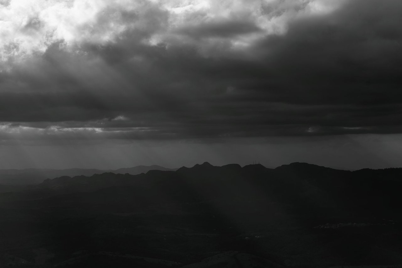 Montanhas de Minas Gerais sob nuvens densas e dramáticas, em uma paisagem em preto e branco.