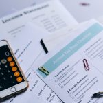 Documentos tributários organizados sobre uma mesa, com checklist, smartphone e calculadora.