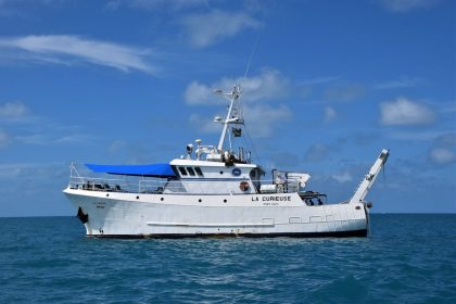 Embarcação de pesquisa La Curieuse navegando em mar aberto sob céu claro.