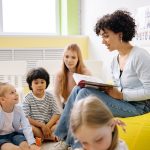 Professora lê um livro para crianças da Educação Infantil em uma sala de aula colorida.