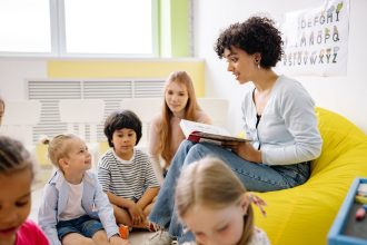 Professora lê um livro para crianças da Educação Infantil em uma sala de aula colorida.