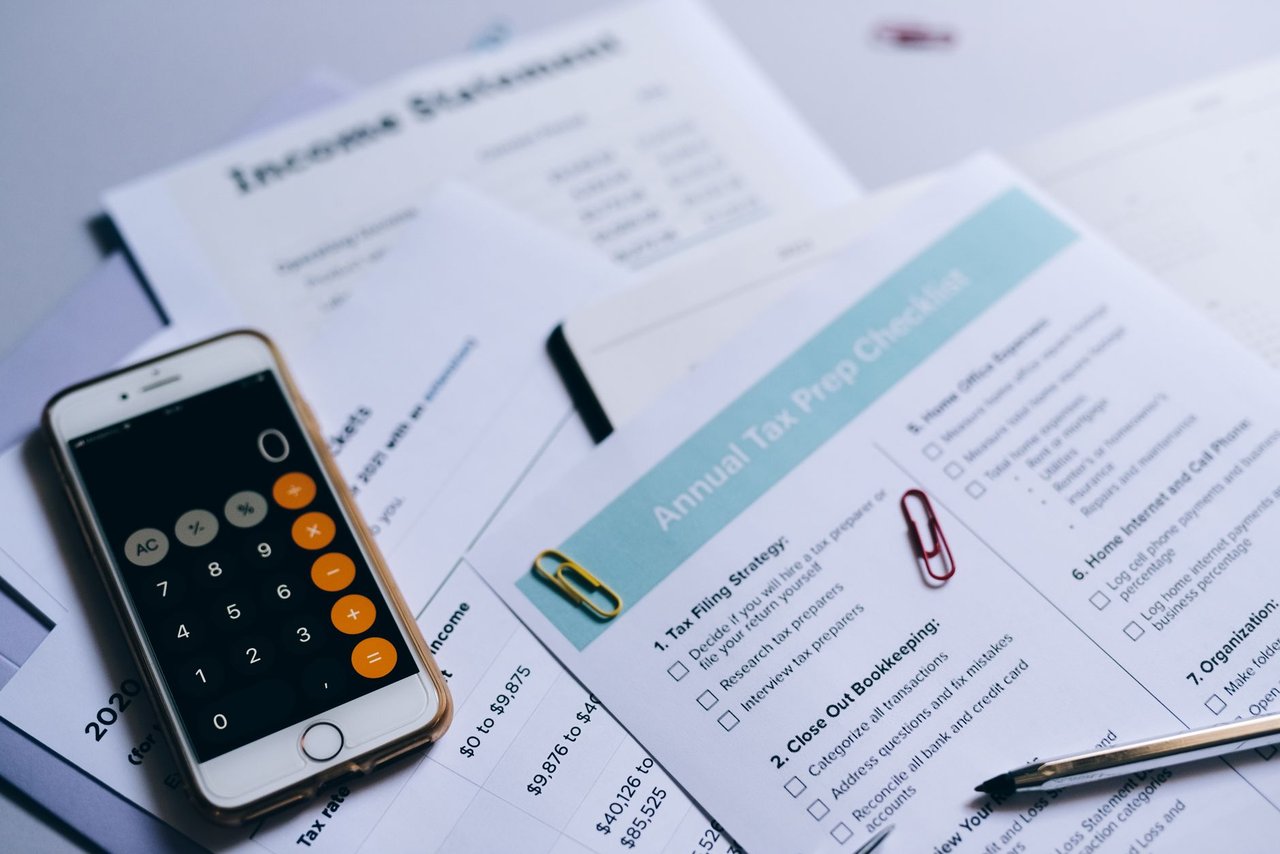 Documentos tributários organizados sobre uma mesa, com checklist, smartphone e calculadora.
